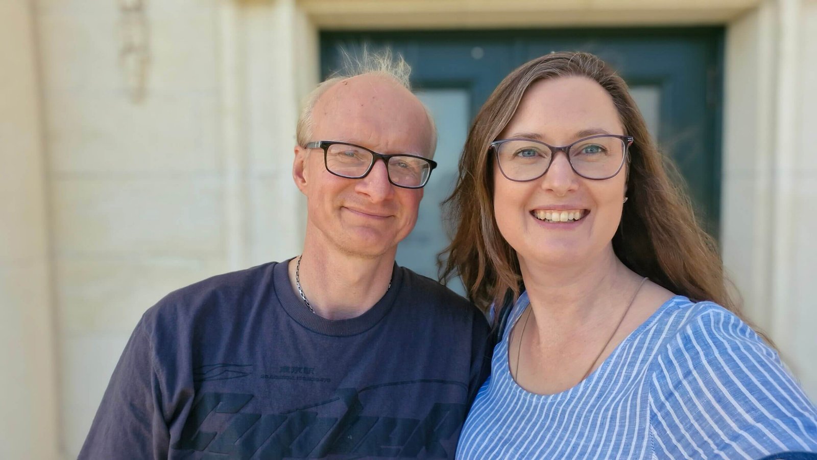 Smiling couple posing for the camera in front of an historic building.