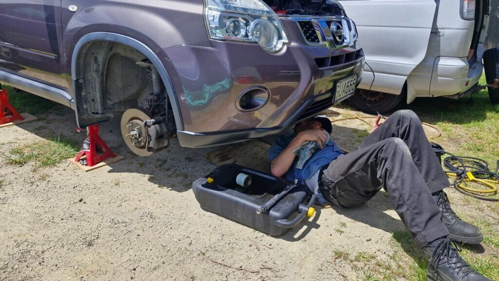 A mechanic lies under a jacked up SUV, completing a service.